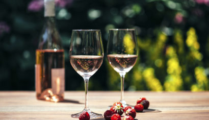 Two glasses of rose wine, wine bottle, strawberries and raspberries on wooden table